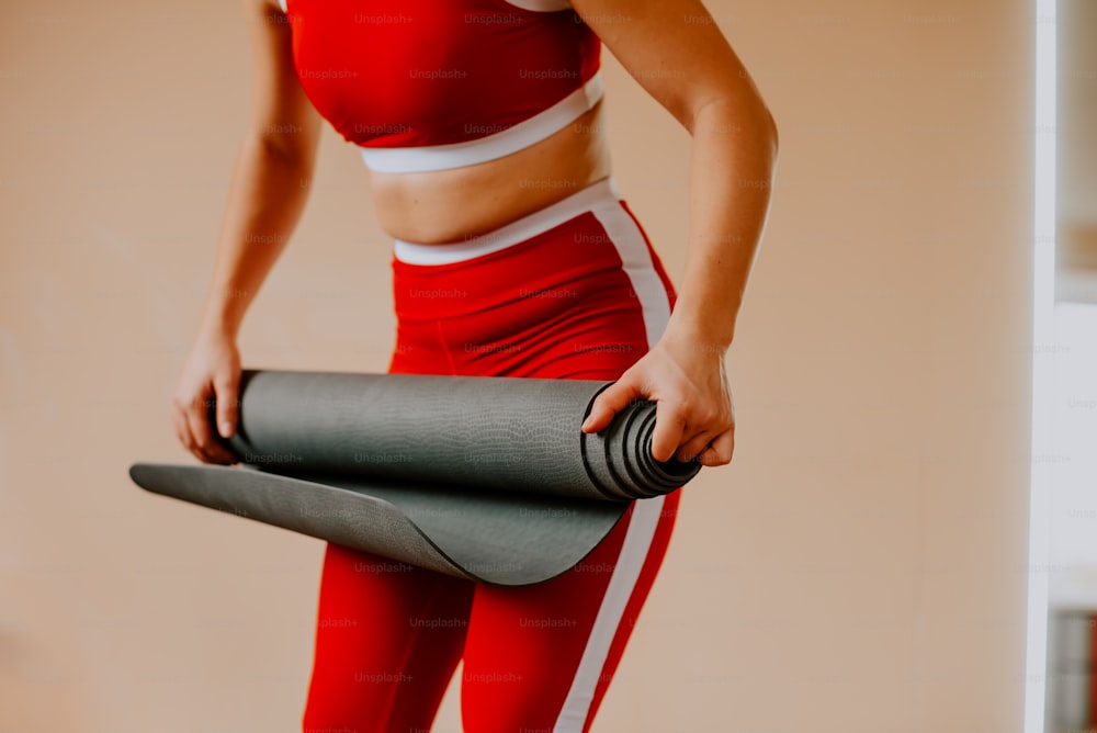 Eine Frau in einem roten Sport-BH-Oberteil, die eine Yogamatte hält