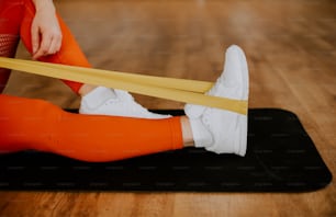 a woman in orange leggings and white sneakers on a black mat