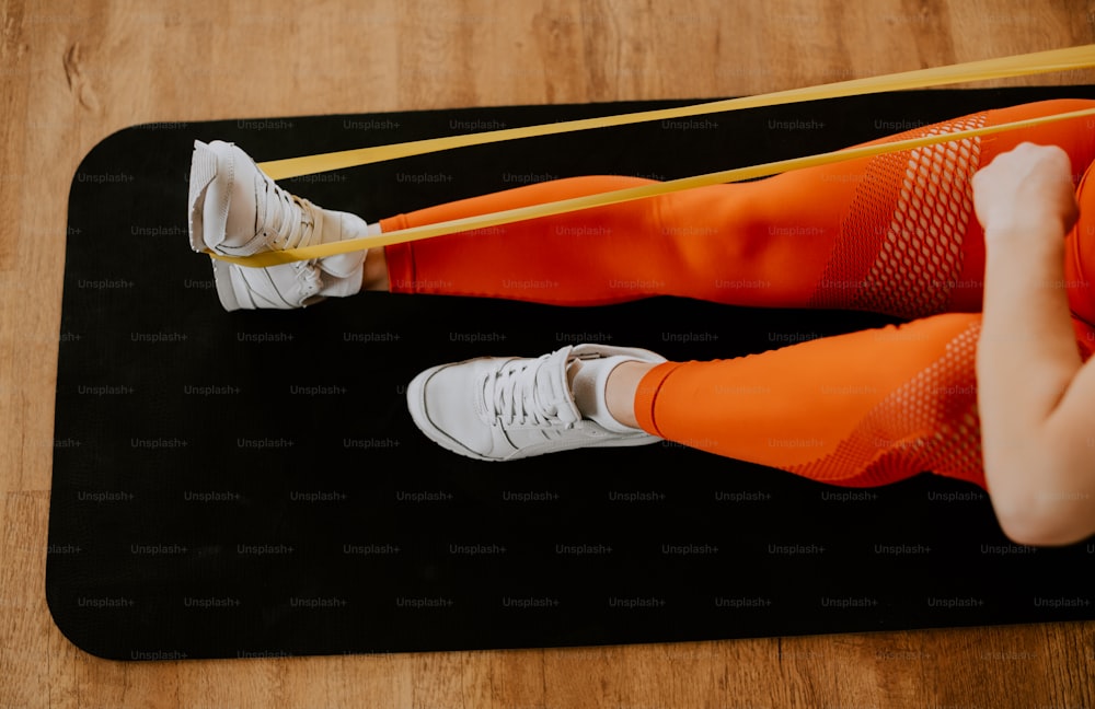 a woman in orange tights and white sneakers on a black mat