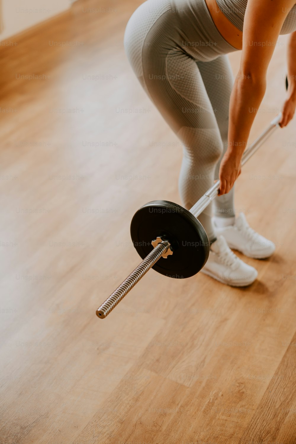 a woman in tights lifting a barbell on a hard wood floor