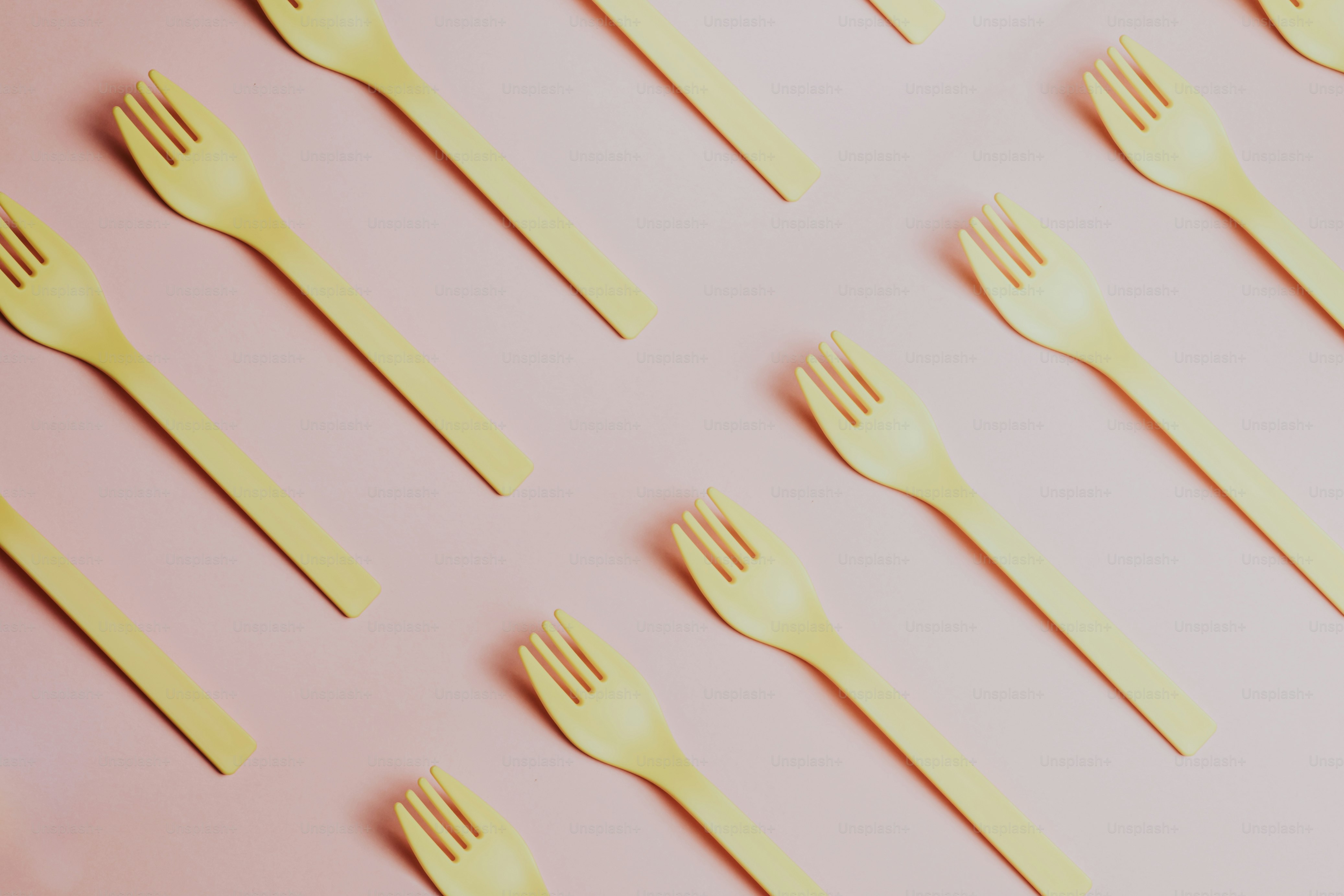 a group of yellow forks and spoons on a pink surface