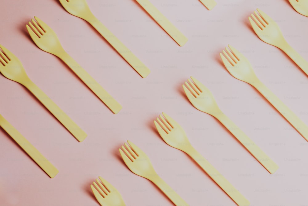 um grupo de garfos e colheres amarelas em uma superfície rosa