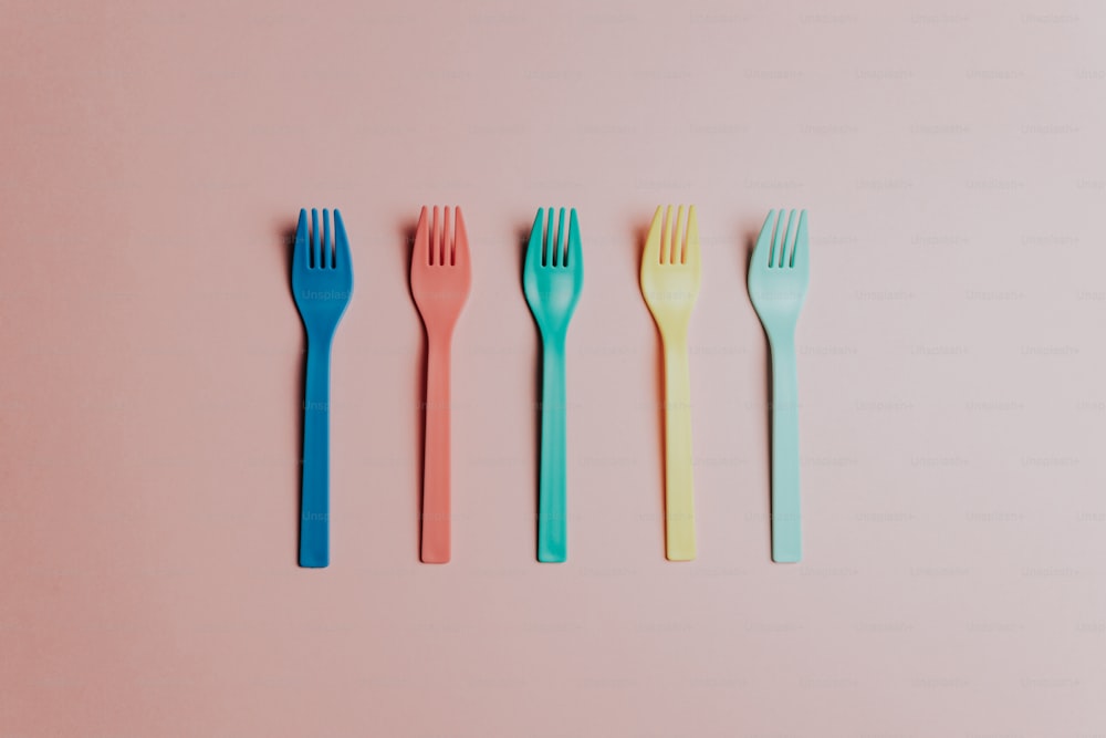 four forks lined up in a row on a pink surface