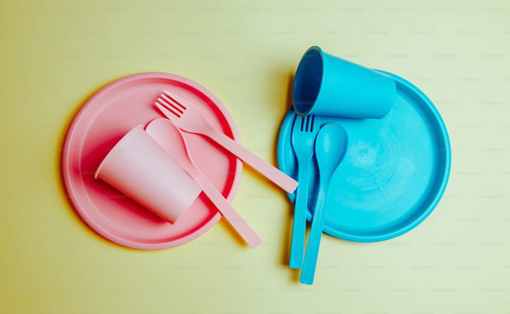 une assiette rose et bleue avec une fourchette en plastique bleu et un gobelet en plastique bleu
