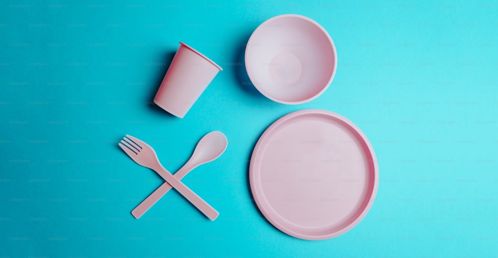 um prato rosa, garfo e copo em um fundo azul