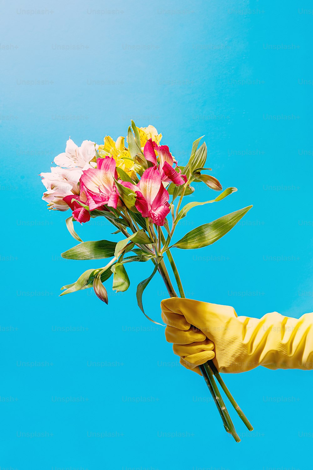 une personne portant des gants de caoutchouc jaunes tenant un bouquet de fleurs