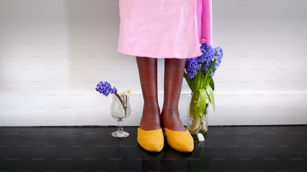 Die Beine einer Frau, die gelbe Schuhe und ein rosa Kleid trägt