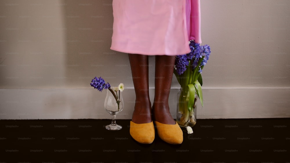 a woman in a pink dress standing next to a vase of flowers