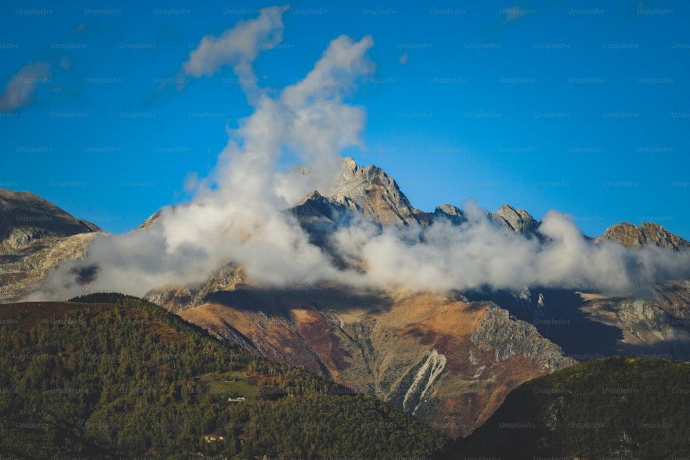 a view of a mountain range with clouds coming out of it