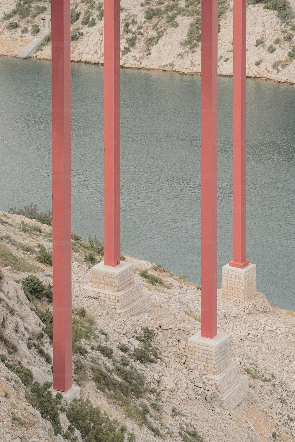 a row of red pillars next to a body of water
