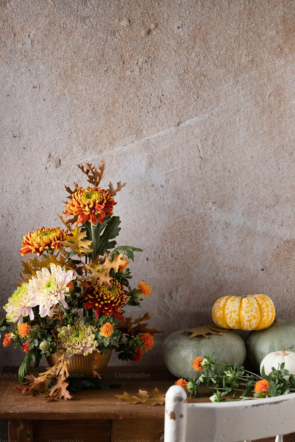 a white chair sitting next to a table filled with flowers and pumpkins