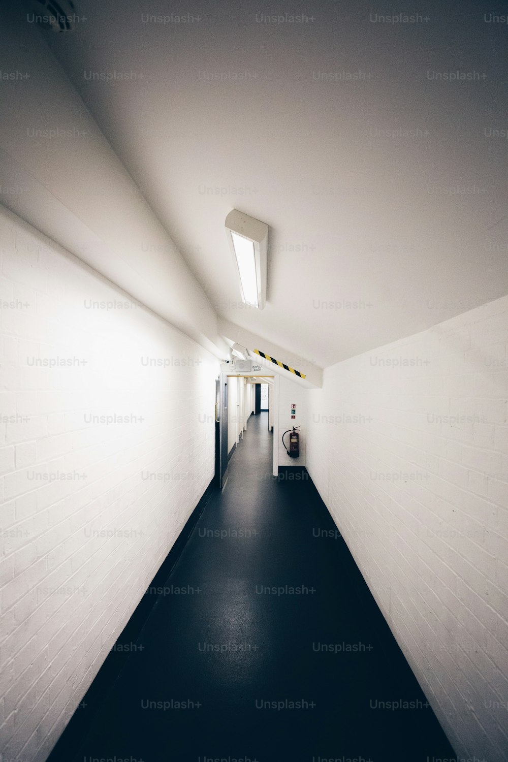 Un largo pasillo con piso negro y paredes blancas