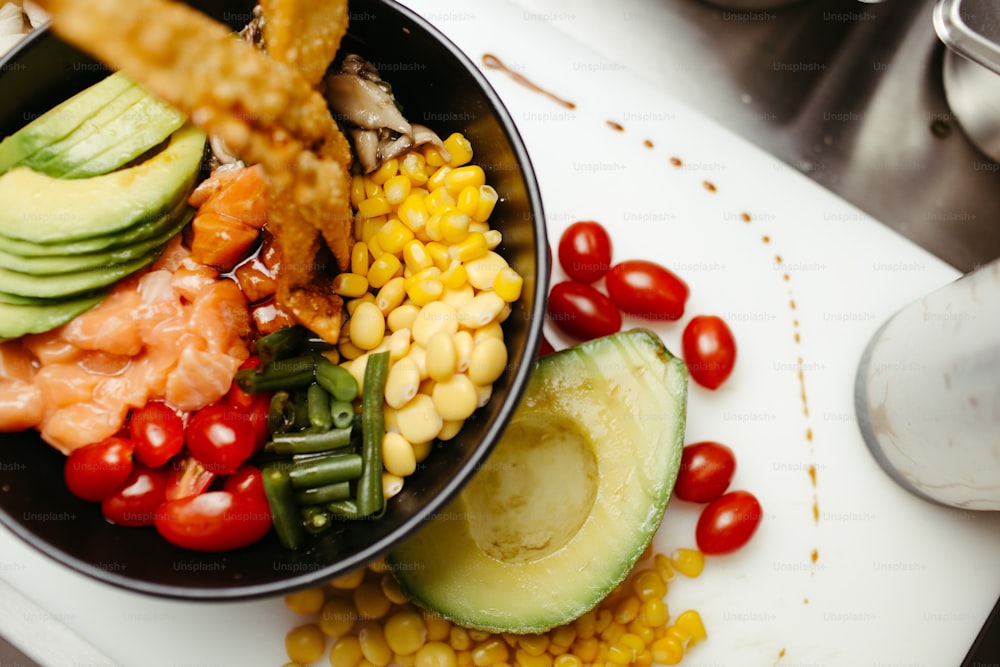 a bowl of food with avocado, tomatoes, corn, and other vegetables