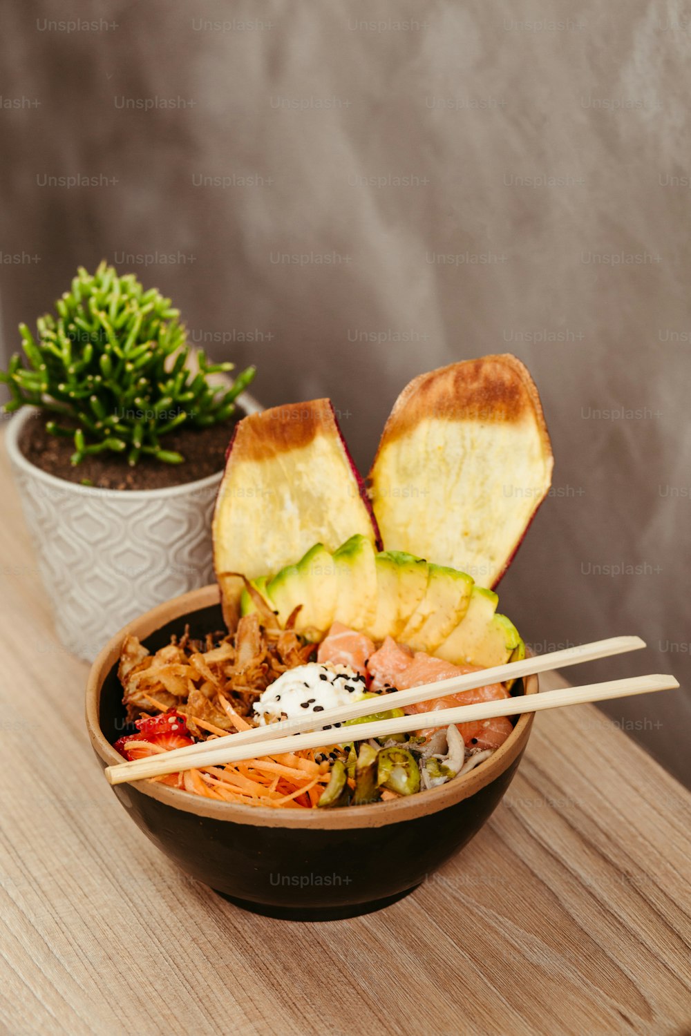 a wooden table topped with a bowl of food and chopsticks