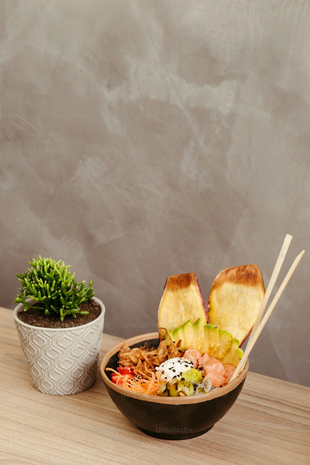 a bowl of noodles with chopsticks next to a potted plant
