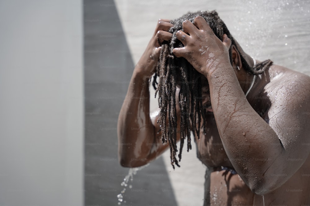 a man with dreadlocks standing under a shower head