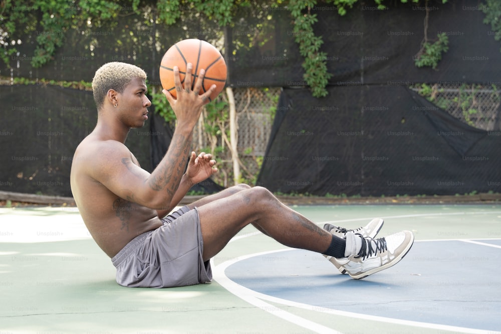 um homem sentado em uma quadra de basquete segurando uma bola de basquete