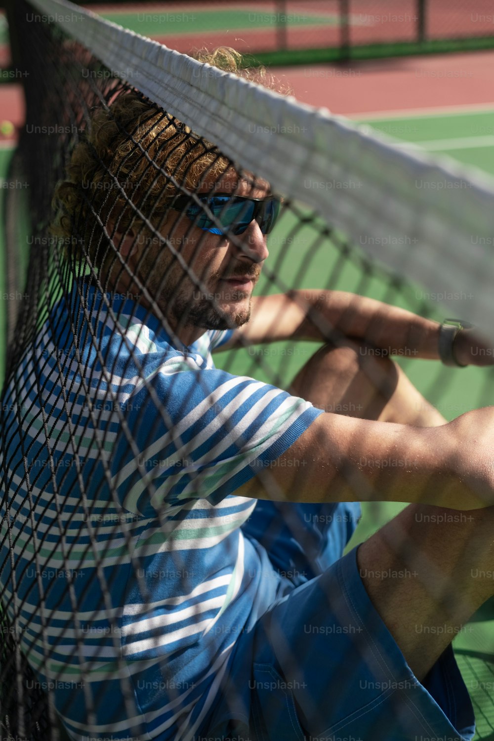 um homem sentado em uma quadra de tênis segurando uma raquete
