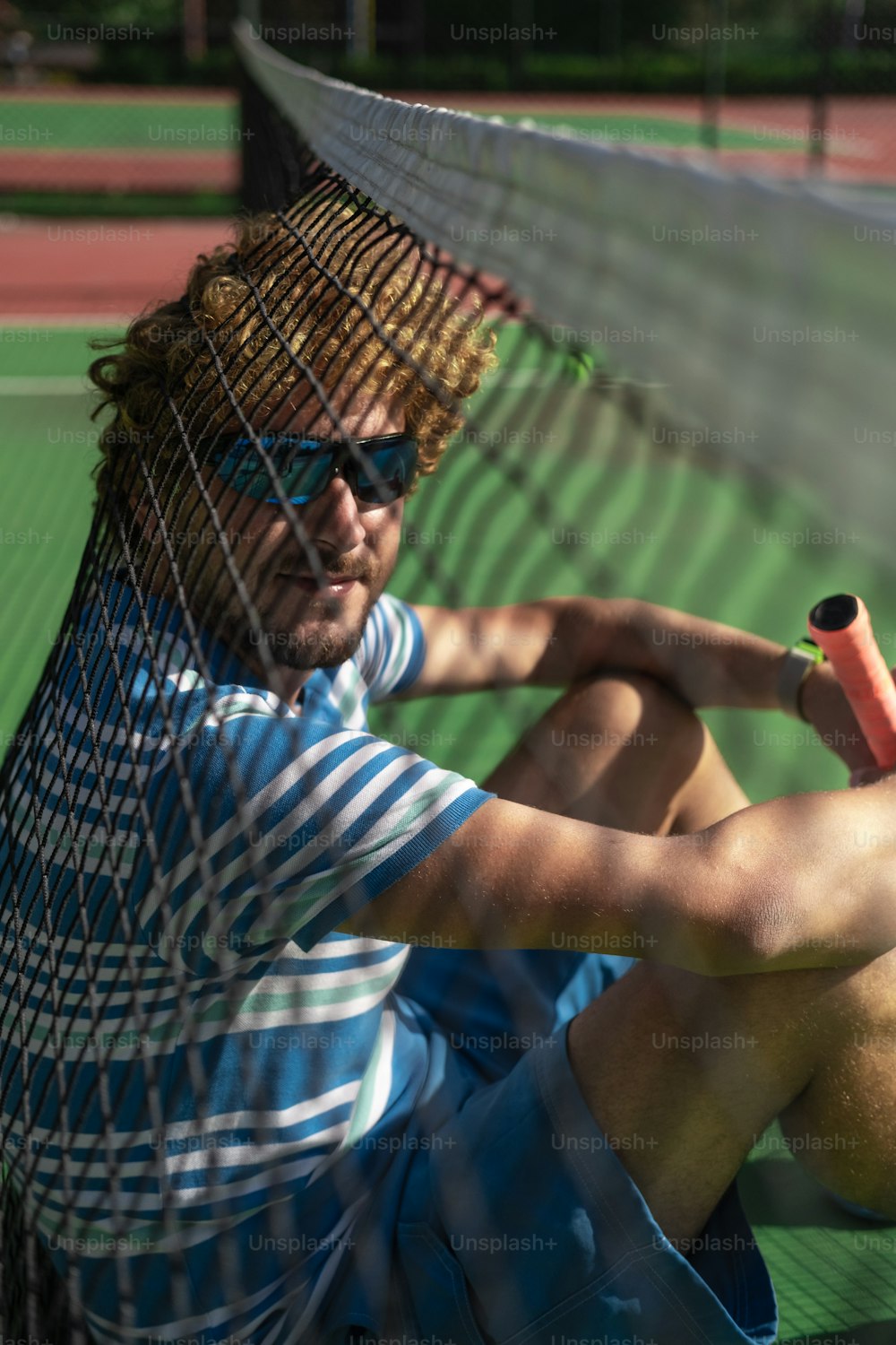 a man sitting on a tennis court holding a racquet