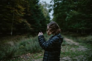 Una mujer parada en un bosque tomando una foto con su teléfono celular