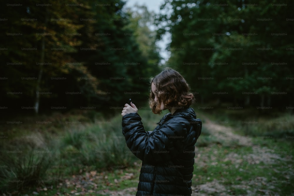 uma mulher em pé em uma floresta tirando uma foto com seu celular