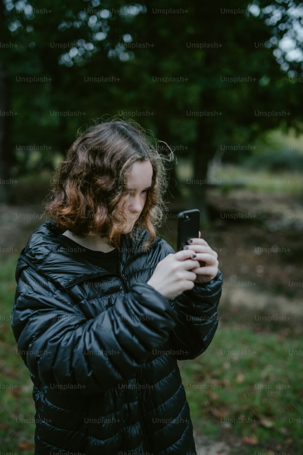 uma mulher de jaqueta preta olhando para o celular