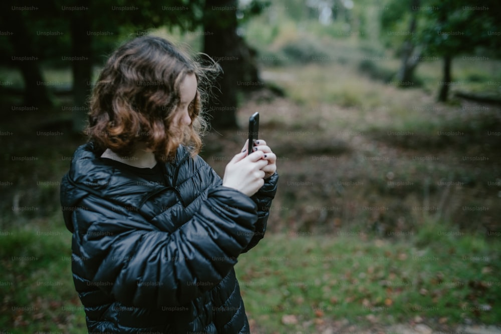 Una mujer parada en un bosque mirando su teléfono celular