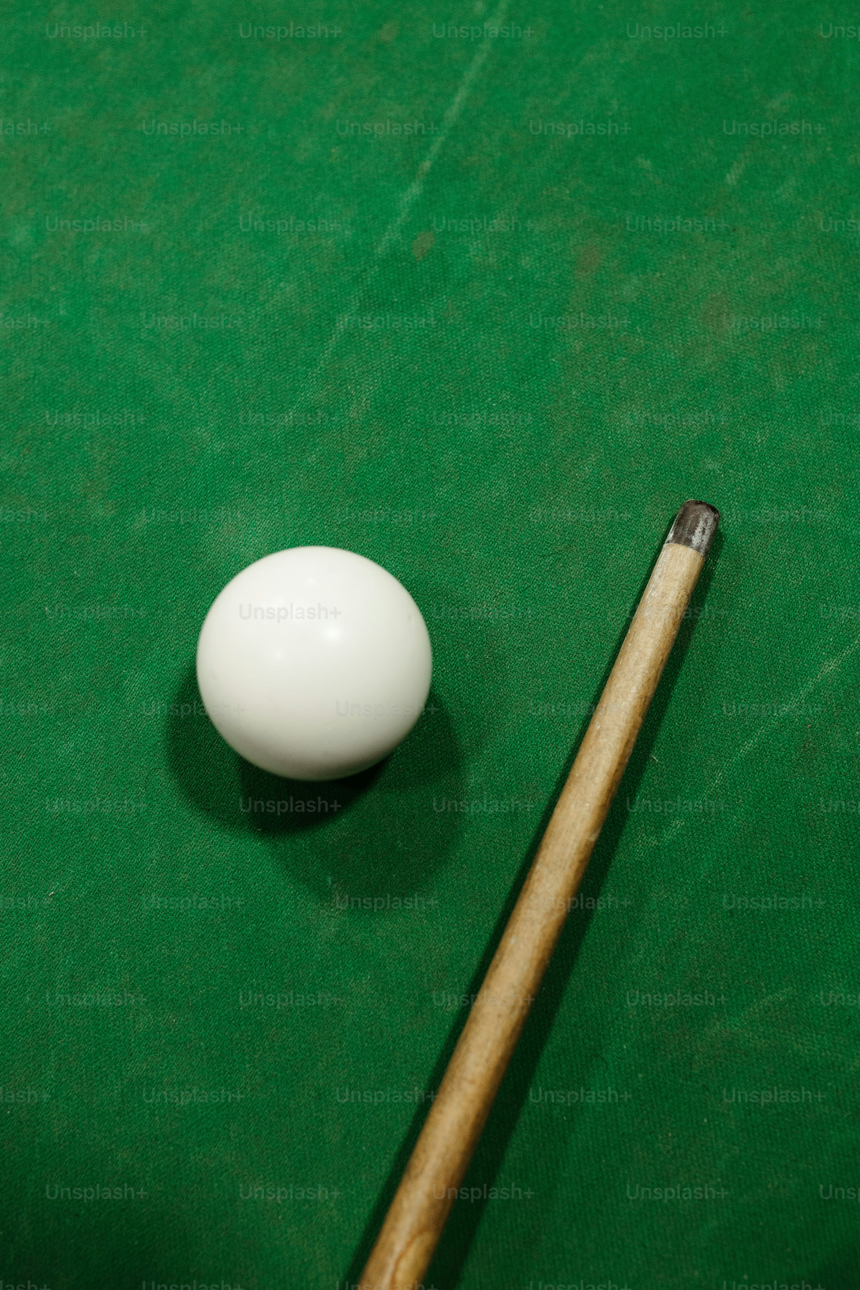 A pool cue and a white ball on a green pool table photo