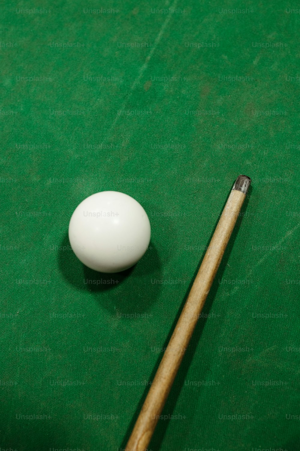 um taco de piscina e uma bola branca em uma mesa de bilhar verde