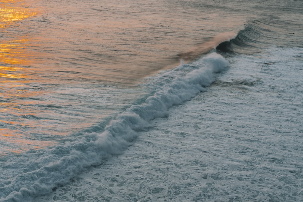 a wave is coming towards the shore at sunset