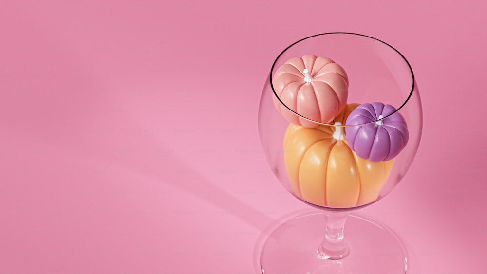 a wine glass filled with colorful pumpkins on a pink background