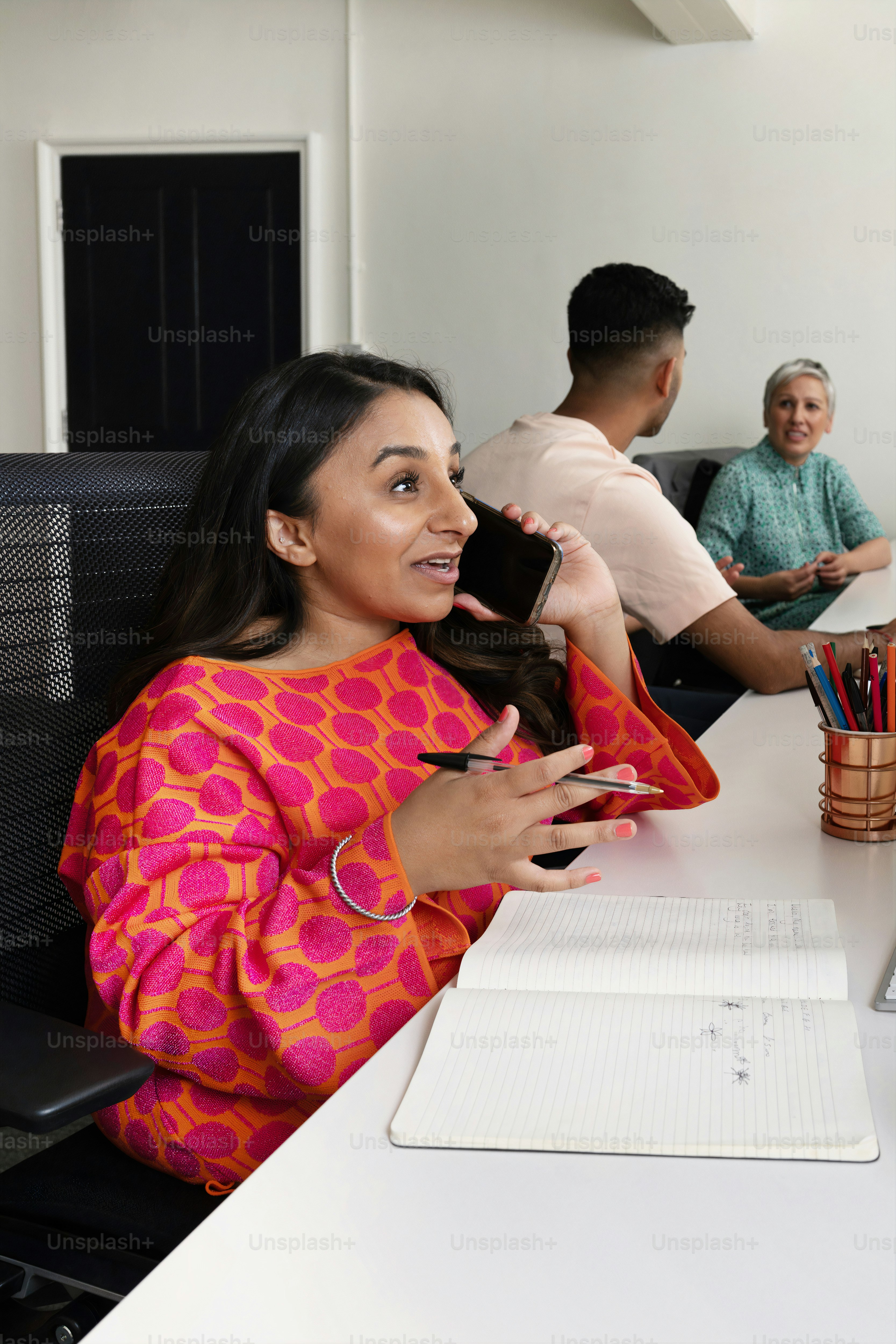 a woman sitting at a desk talking on a cell phone