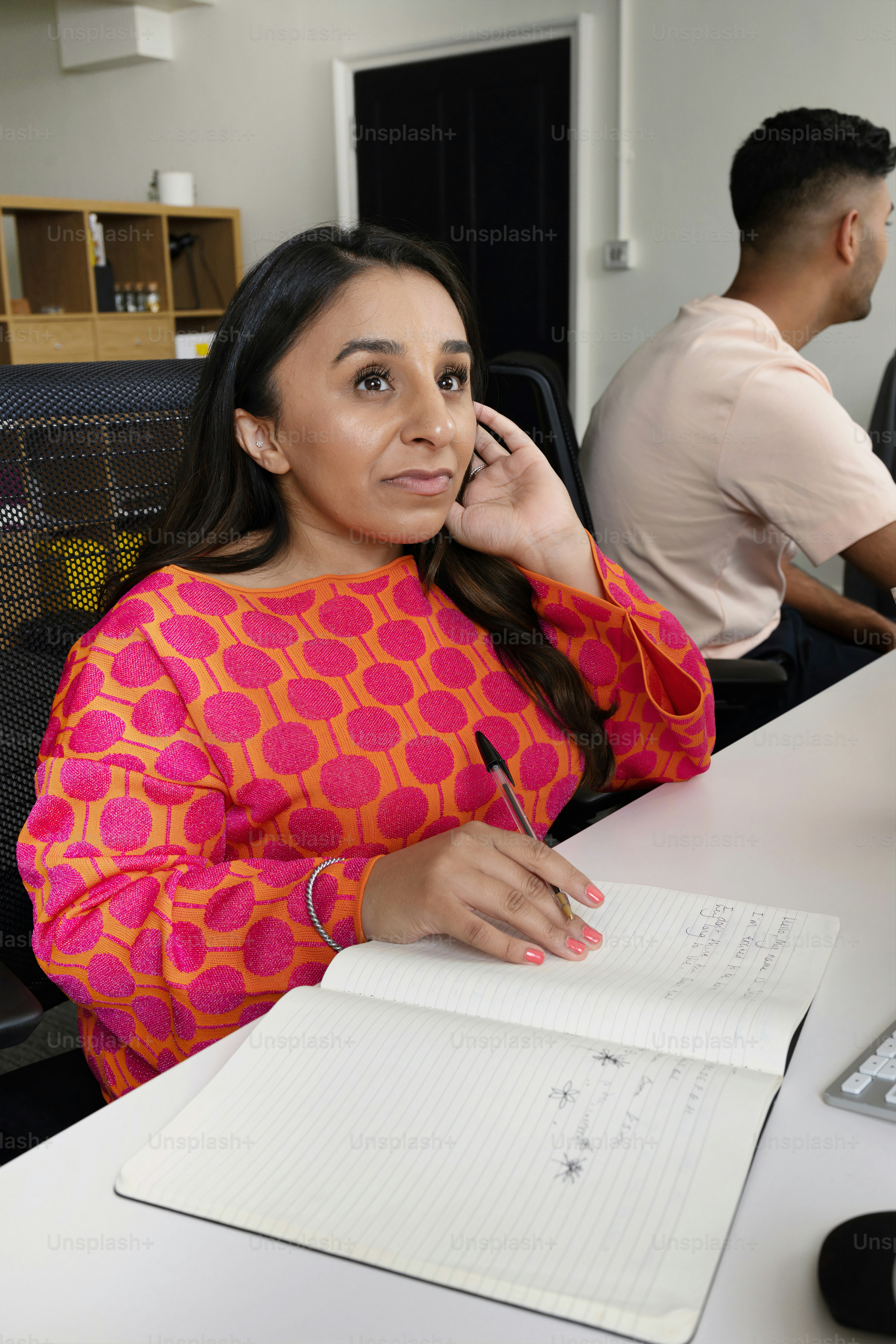a woman sitting at a desk talking on a cell phone