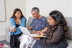 three women sitting on a couch looking at a book