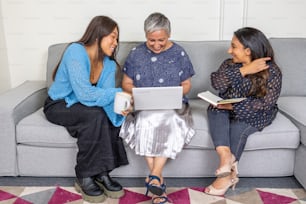 three women sitting on a couch looking at a laptop