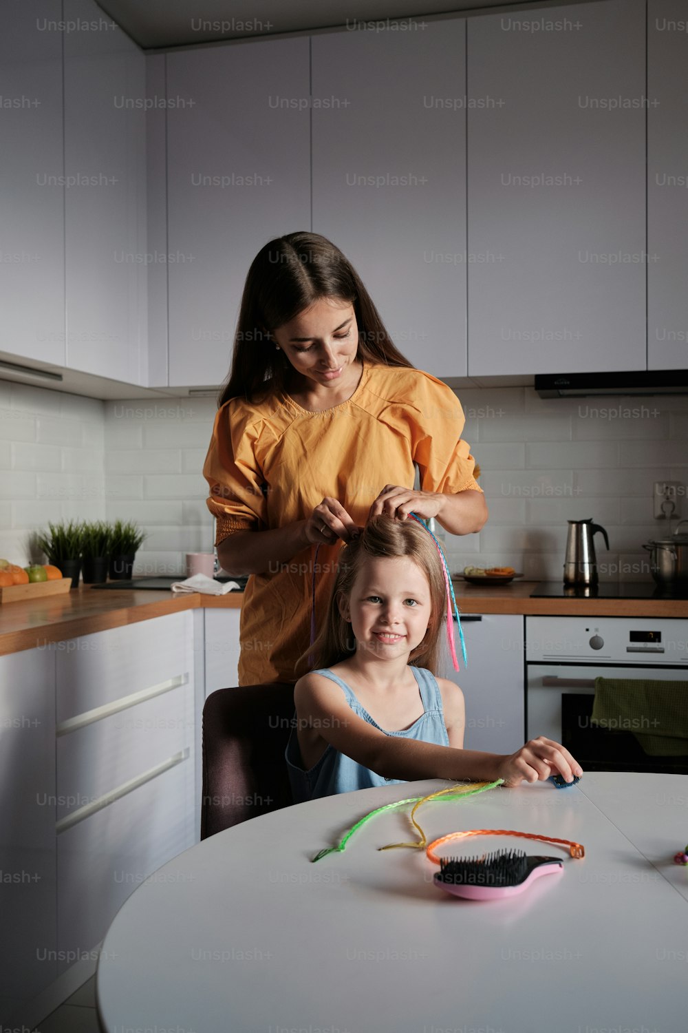 a woman combing a little girl's hair in a kitchen