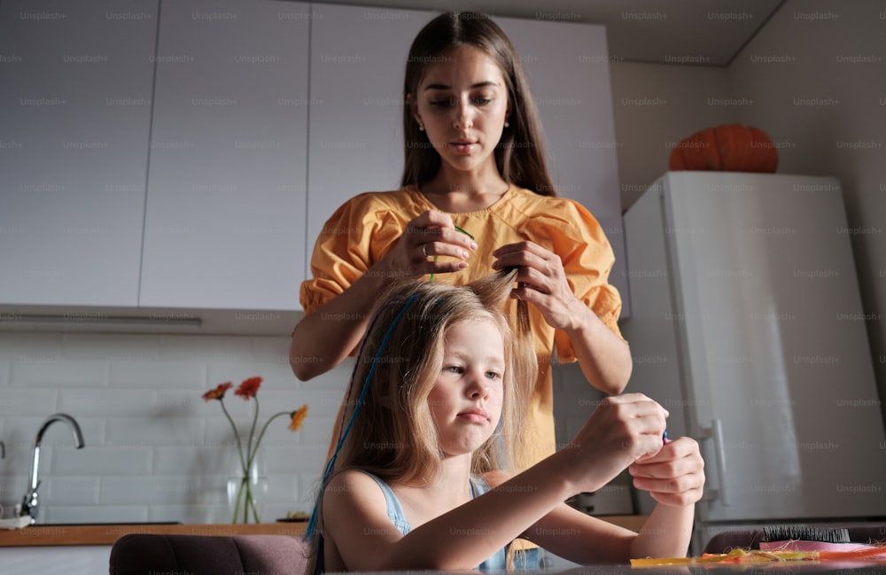 a woman cutting a little girl's hair in a kitchen