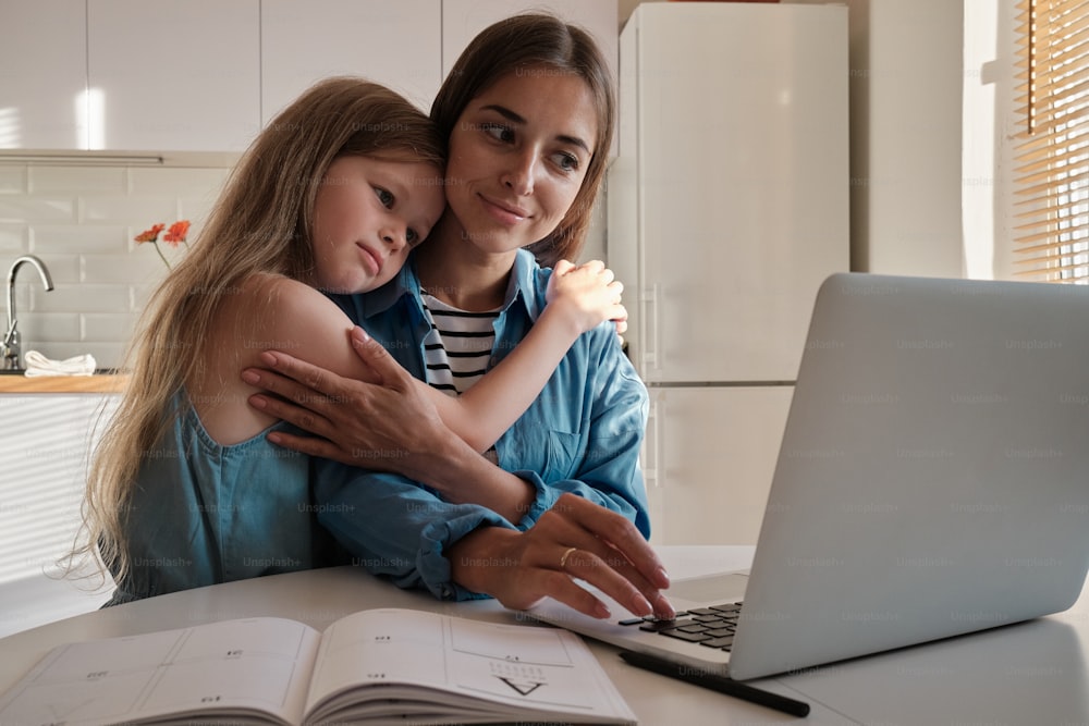 a woman hugging a little girl in front of a laptop