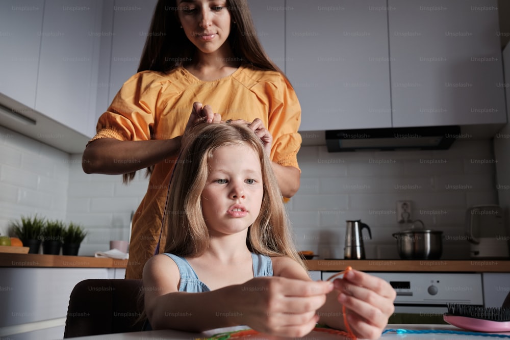 a woman combing a little girl's hair in a kitchen