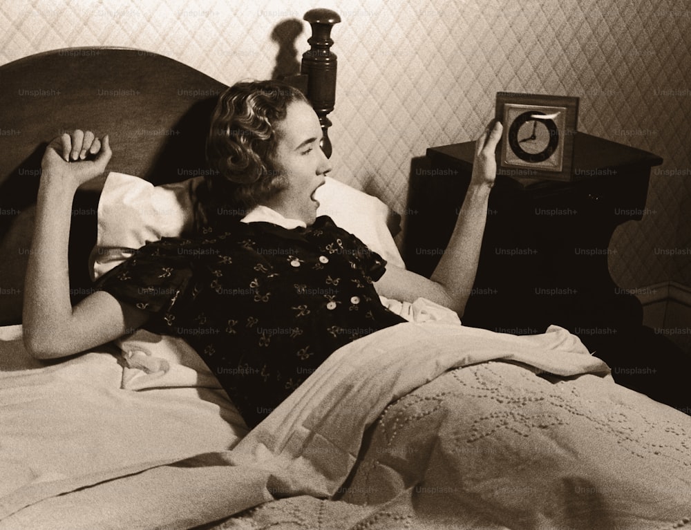 a woman laying in bed with a clock on the nightstand