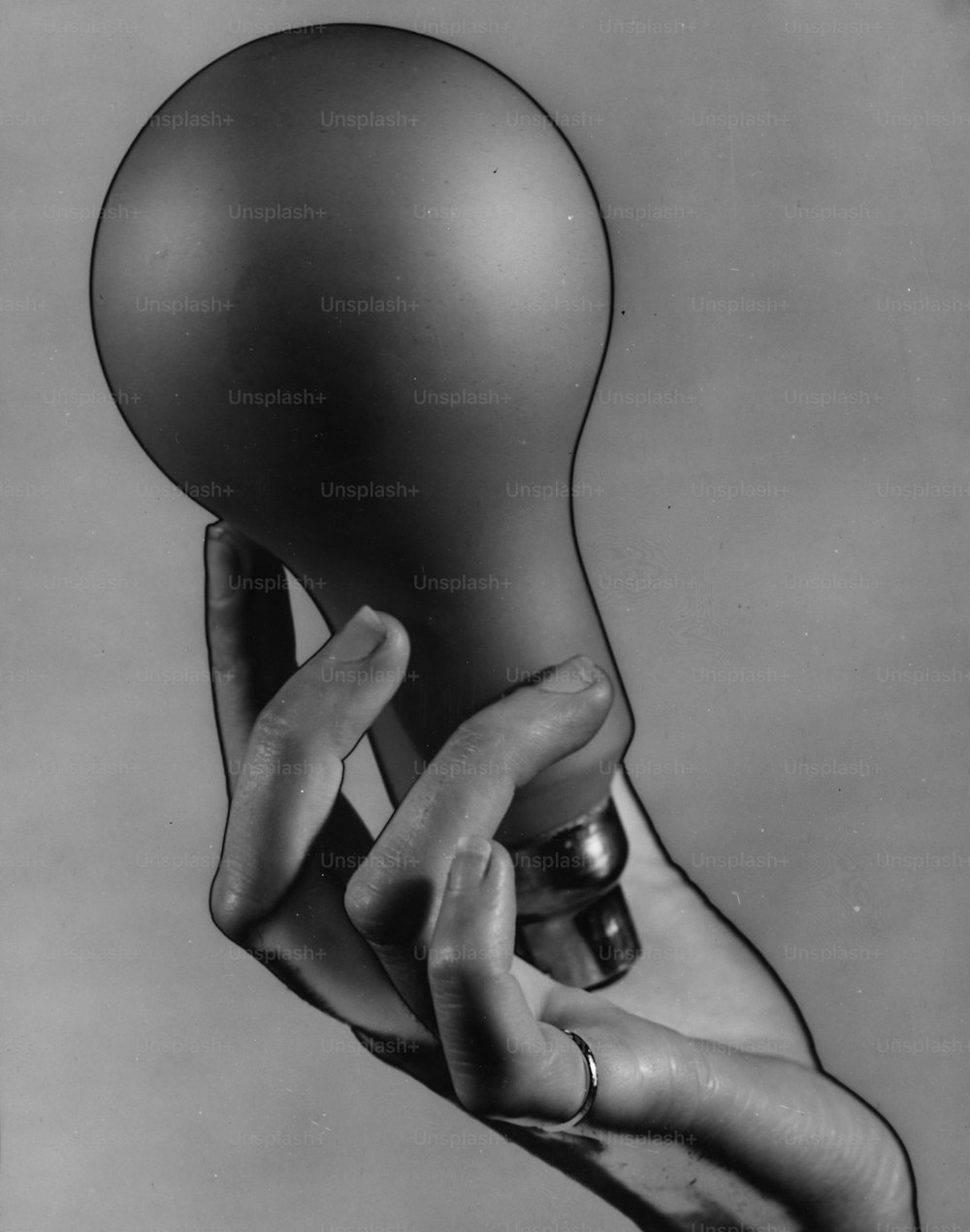 Hacia 1936: Una sola mano con un anillo en el dedo meñique, sosteniendo una gran bombilla eléctrica.  Imagen solarizada.  (Foto de Chaloner Woods/Getty Images)