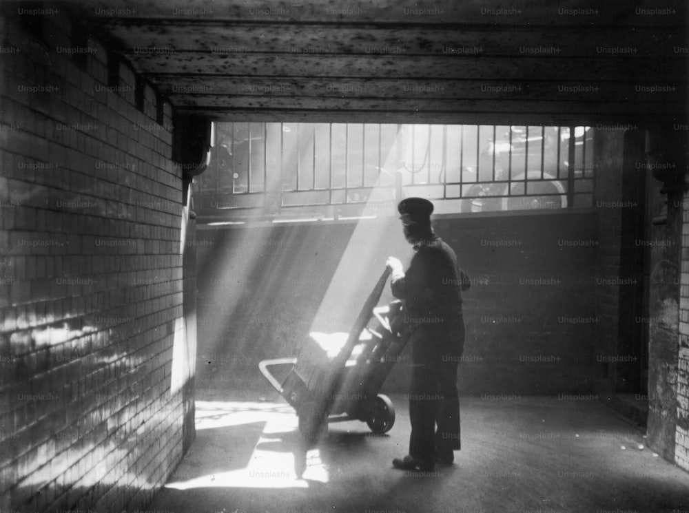 1938 circa: un facchino ferroviario che spinge il suo carrello attraverso un raggio di sole.  (Foto di Chaloner Woods/Getty Images)