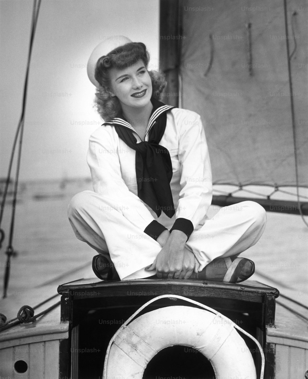UNITED STATES - CIRCA 1950s:  Woman in sailor outfit sitting on sailboat.