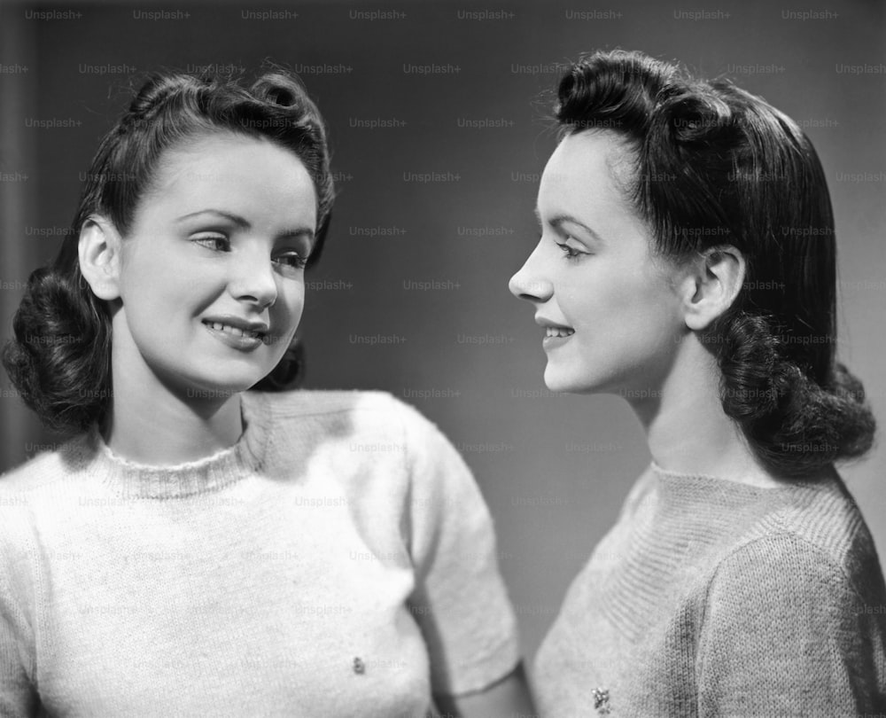 UNITED STATES - CIRCA 1950s:  Twin sisters wearing sweaters.