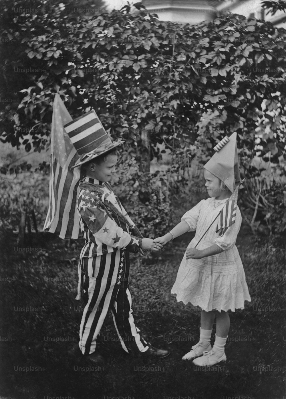 Ein Junge und ein Mädchen in patriotischen Kostümen des vierten Juli, geben sich die Hand, um 1925. (Foto von Paul Thompson / FPG / Archivfotos / Getty Images)