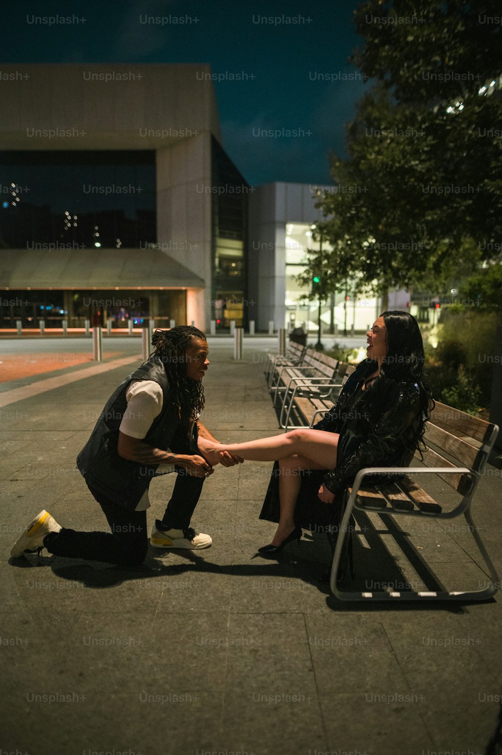 a man kneeling down next to a woman on a bench
