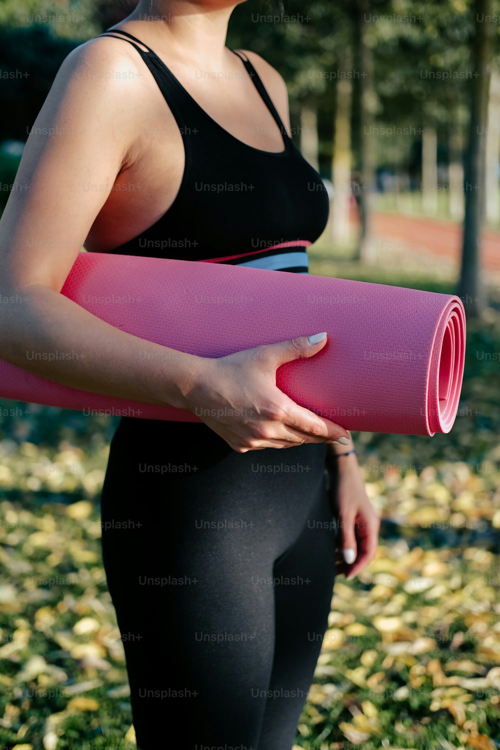 a woman holding a pink yoga mat in a park