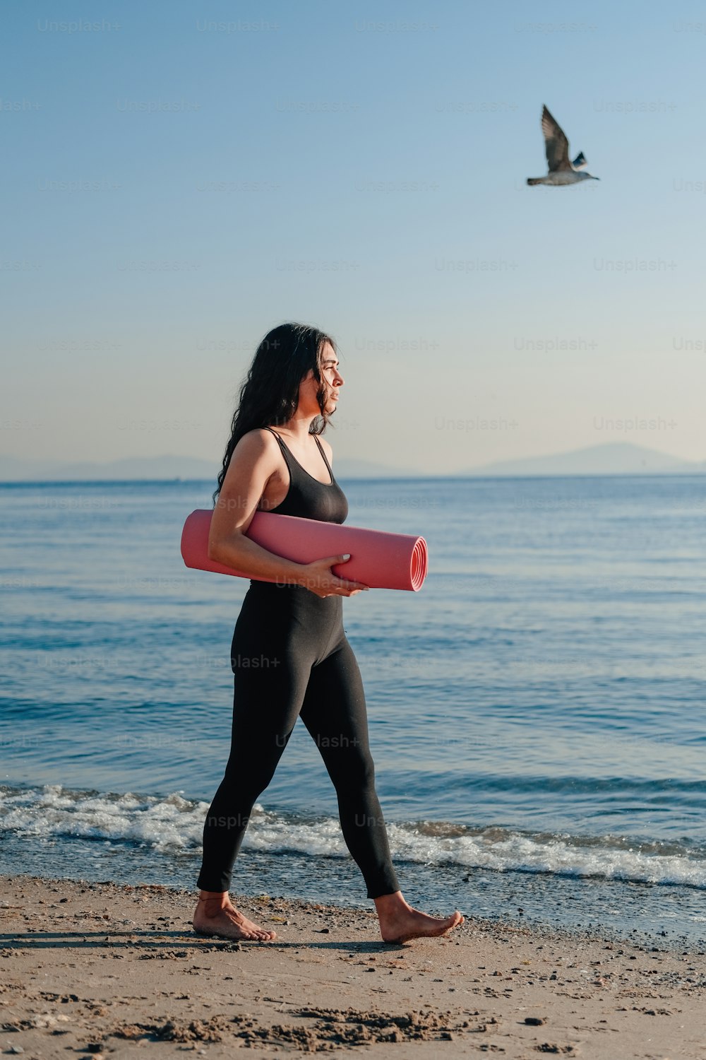 a woman walking on a beach carrying a pink surfboard