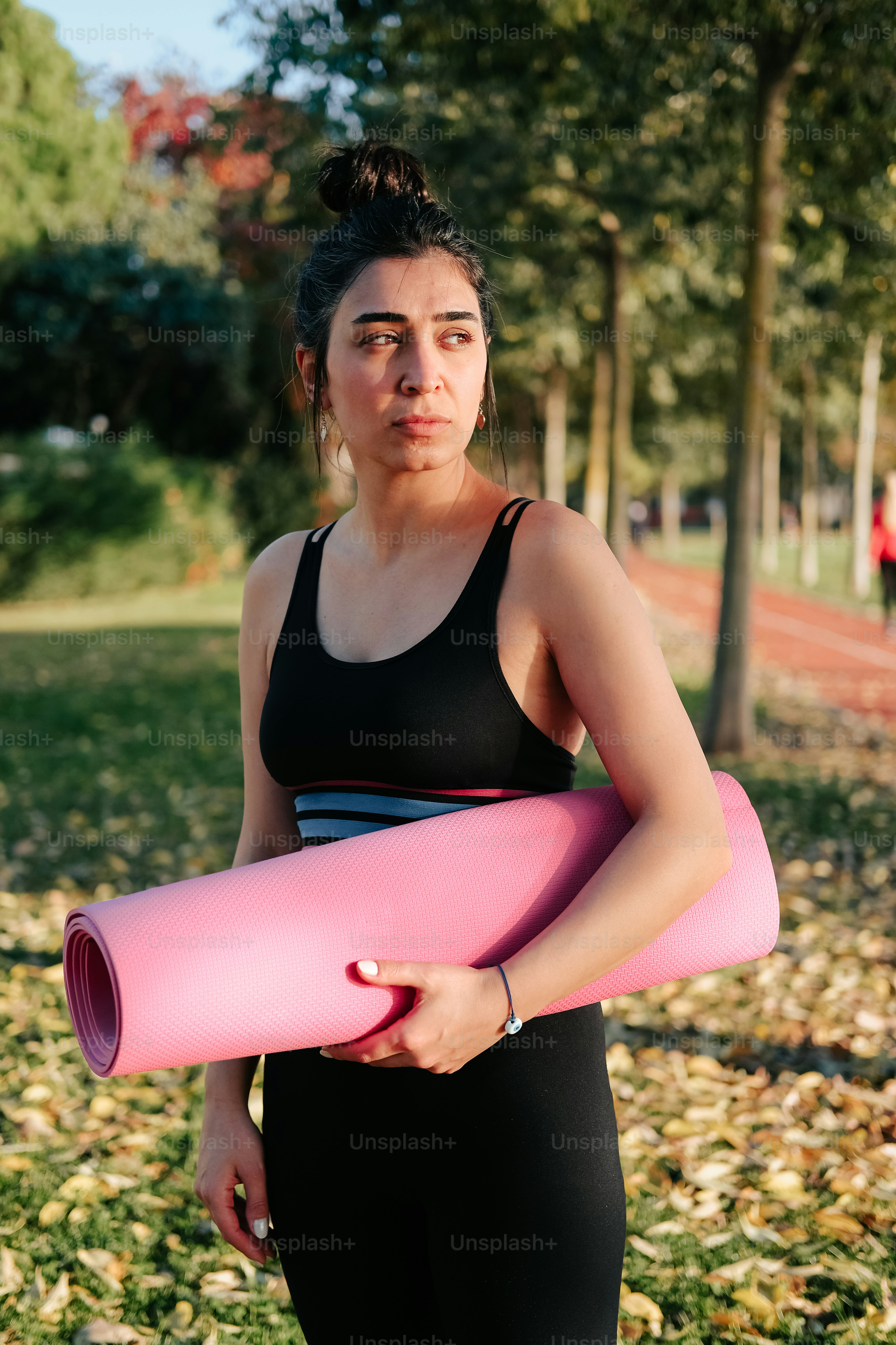 eine frau, die eine rosa yogamatte in einem park hält