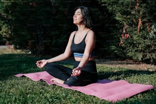 Una mujer sentada en una esterilla de yoga rosa en un parque